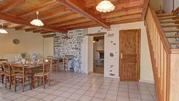 A spacious dining area with a wooden table and chairs, a stone wall, and a staircase leading to an upper level.