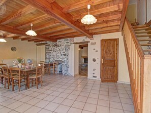 Un vaste espace dédié à la salle à manger, avec une table et des chaises en bois, un mur en pierre et un escalier menant à un niveau supérieur.