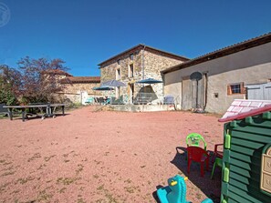 Une cour avec un bâtiment en pierre, des sièges en plein air et un espace de jeux.