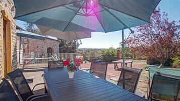 An outdoor patio with a table and chairs, a large umbrella, and a stone building in the background.