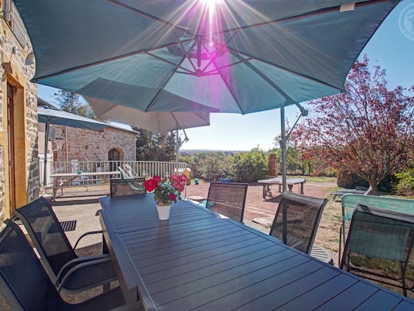 Un patio al aire libre con una mesa y sillas, un paraguas grande y un edificio de piedra al fondo.