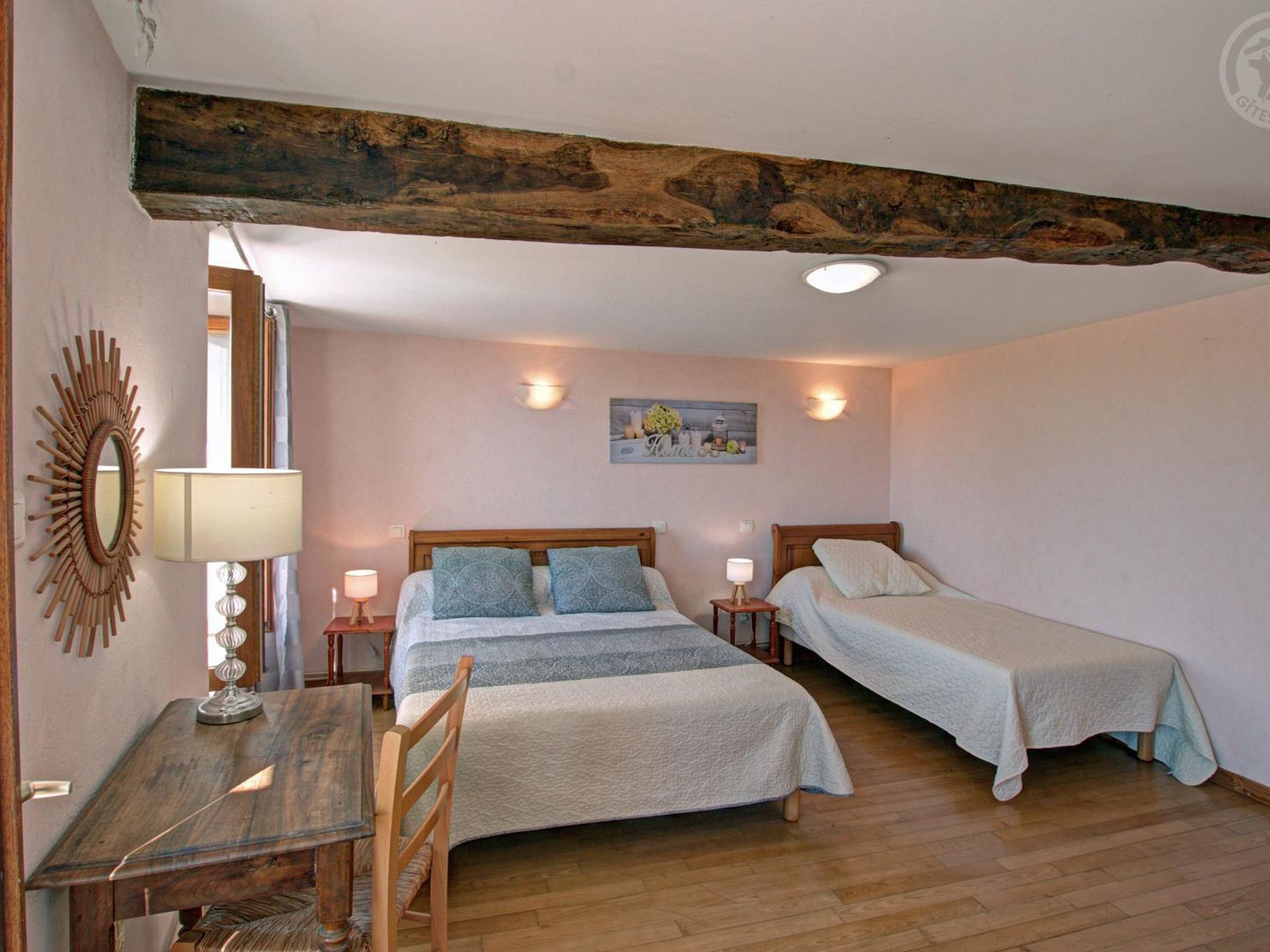 A bedroom with a wooden ceiling, two beds, a desk, and a chair.