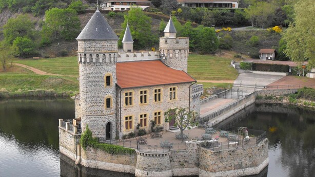Una construcció al estil d'un castell, amb fossat, parets de pedra i teulada de teules vermelles.