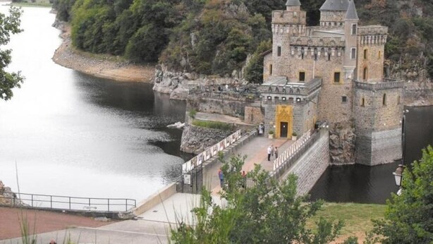 Un château historique, doté de douves, situé sur une colline surplombant une rivière.