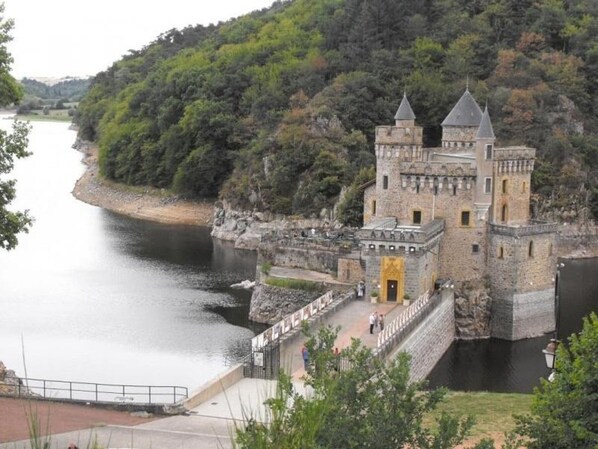 Un castello storico con fossato, affacciato su una collina e che domina un fiume.