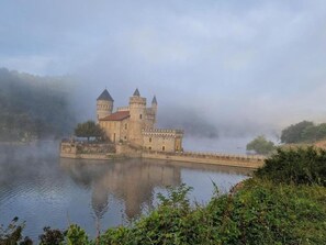 Un castello storico con due torri, affacciato su una sponda fluviale avvolta nella nebbia.