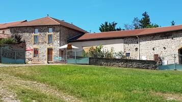 Un bâtiment en pierre avec un toit recouvert de tuiles rouges, un chemin pavé et une pelouse devant.