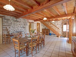 Un comedor amplio con pared de piedra, vigas de madera en el techo y una escalera que lleva a un nivel superior.