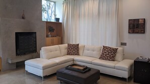 Ein modernes Wohnzimmer mit einem Ecksofa, einem Kamin und einem großen Fenster mit Vorhängen.