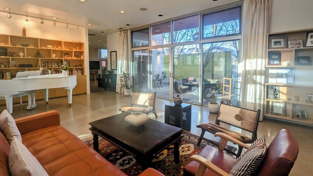 Ein geräumiges Wohnzimmer mit Klavier, Ledersofas, einem Couchtisch und einem großen Fenster mit Blick ins Freie.