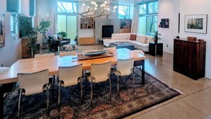 Ein geräumiges Wohnzimmer mit großem Holzesstisch, bequemen Sitzmöglichkeiten, einem Kamin und großen Fenstern.