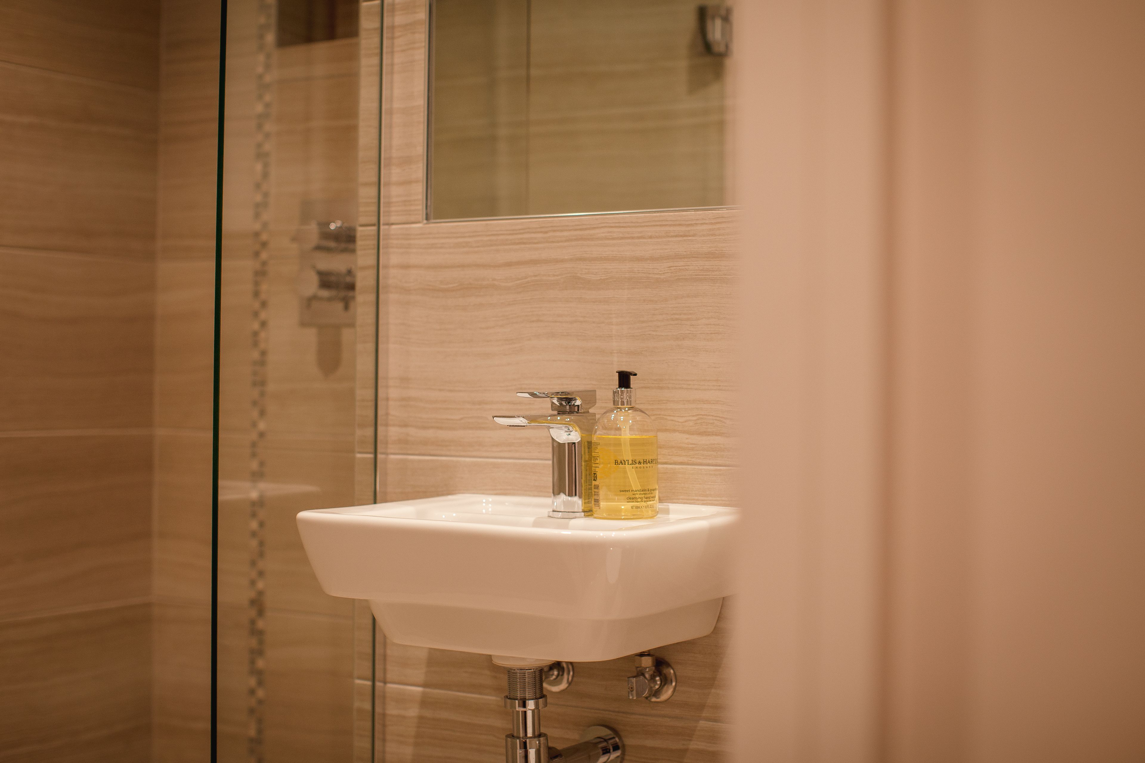 A bathroom with a glass shower enclosure, a white sink with a chrome faucet, and a bottle of hand soap.
