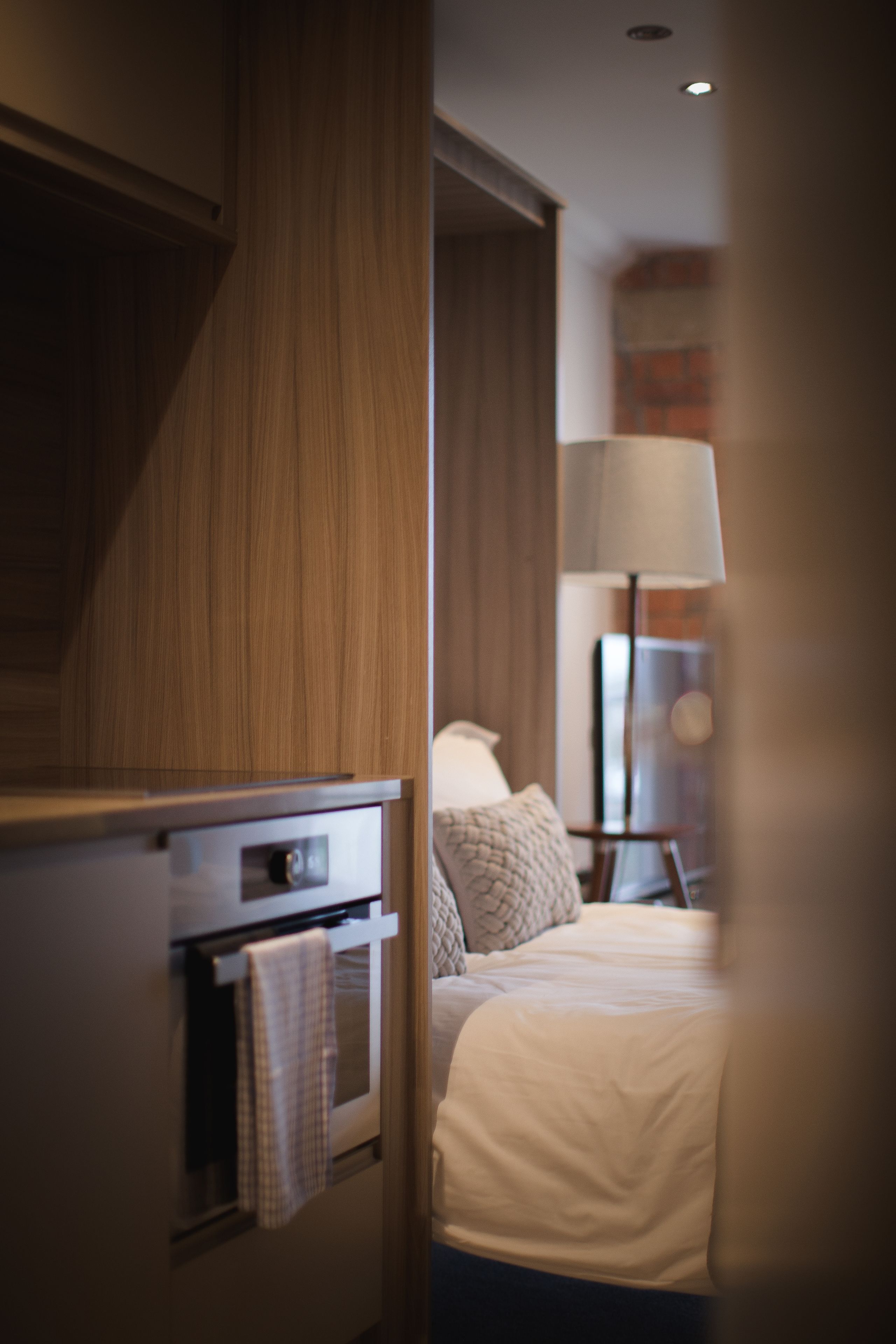 Une chambre d’hôtel avec une armoire en bois, un lit recouvert d’une couette blanche, une lampe et une petite table avec une lampe.