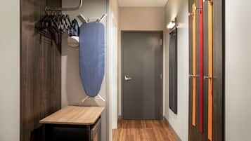 A hallway with a wooden table, a blue ironing board, and a door with colorful vertical stripes.
