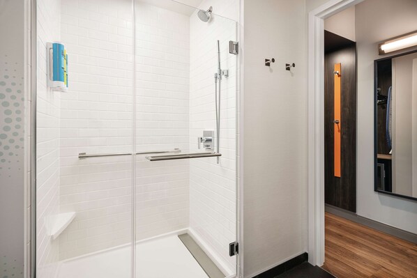 A modern bathroom with white tiled walls, a glass shower enclosure, and a wooden floor. - Tru By Hilton Denver Downtown Convention Center (Denver)