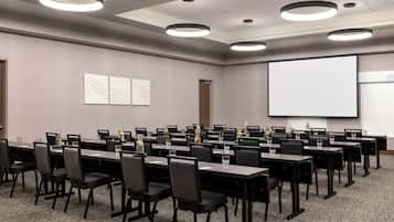 Ein Konferenzraum mit mehreren Tischen und Stühlen, einer Projektionsleinwand und einer Whiteboard.