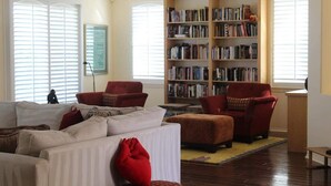 A living room with a beige sofa, red armchairs, a bookshelf, and a wooden floor. - Four Seasons Stunner (Palm Springs)