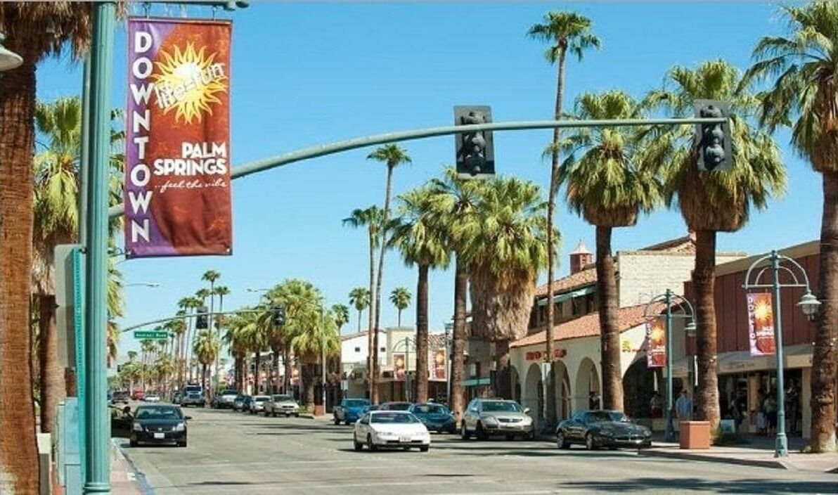 Straßenansicht mit Palmen, einem 'Downtown Palm Springs'-Schild und blauem Himmel.