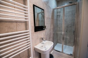 A bathroom with a glass-enclosed shower, a white sink, and a towel rack. - 50 Bootham Crescent (York)