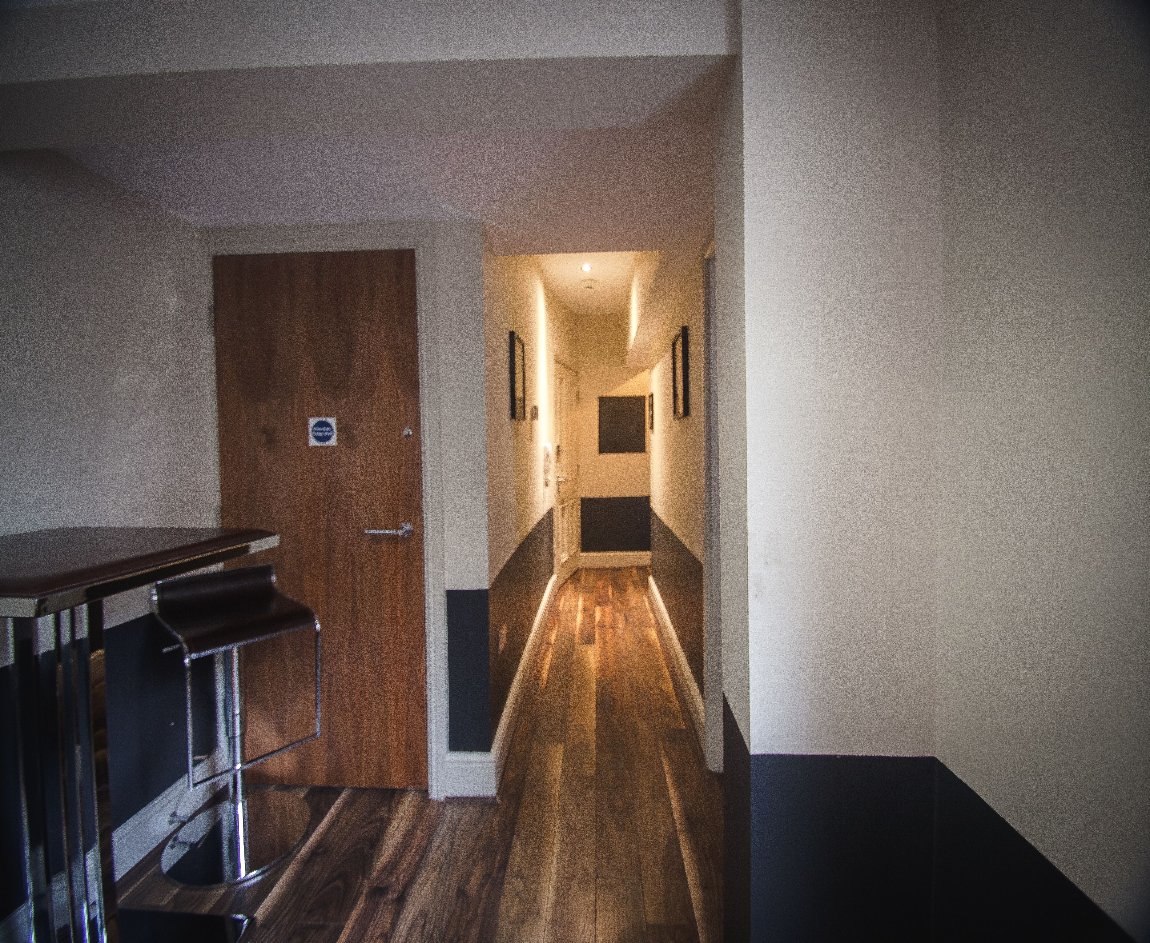 A hallway with a wooden floor, a door, and a small table with a metal frame.