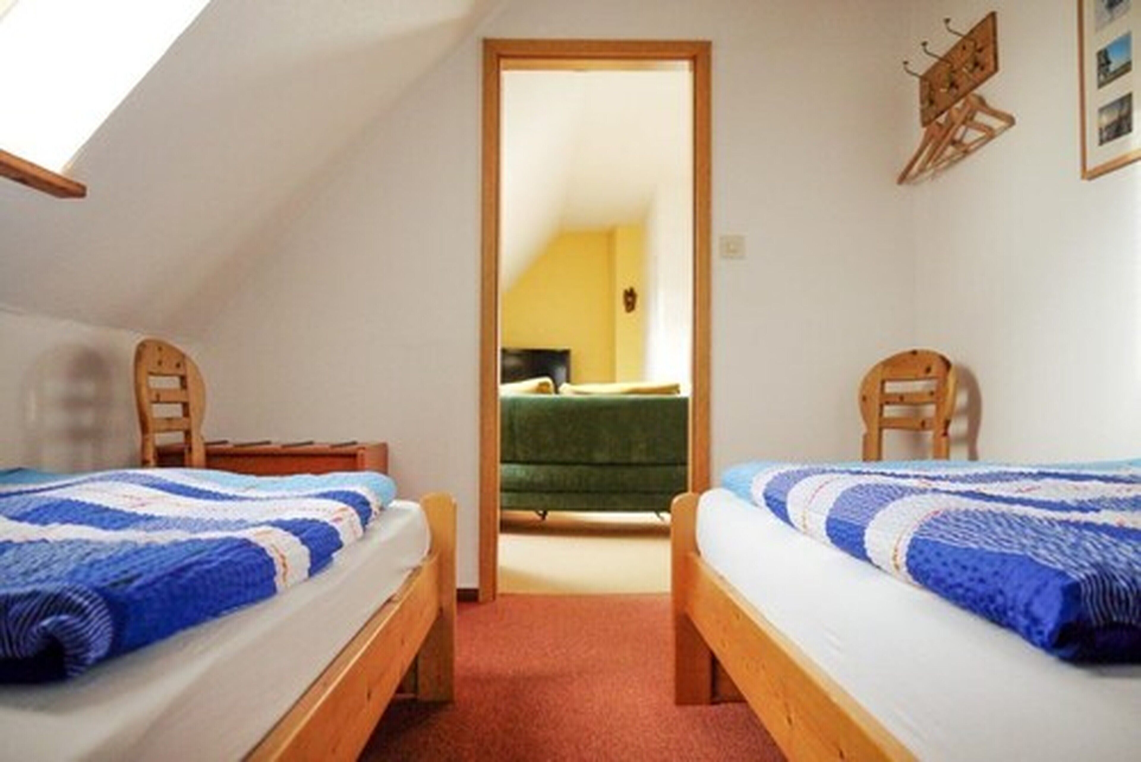 A room with two beds, a wooden door, and a view into another room with a green sofa.