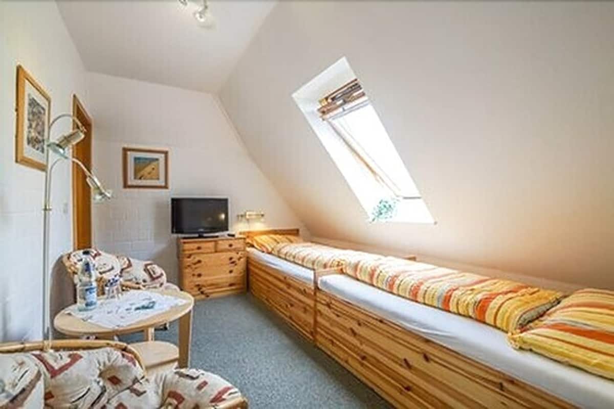 Una habitación pequeña y acogedora con una cama individual, un escritorio, una silla y un televisor.