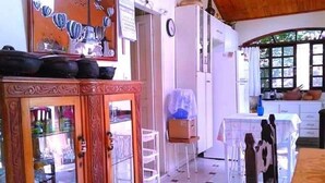 A room with a wooden cabinet, a white refrigerator, a small table, and a window with a view of greenery. - OUR PARADISE available Christmas New Year <br>End of March holiday promotion 981113133 (Arujá)