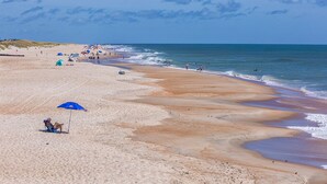 A wide sandy beach with gentle waves, a clear sky, and a few people and umbrellas. - Semi-Soundfront Home with Private Pool, Hot Tub, Elevator, and Home Theater (Hatteras)