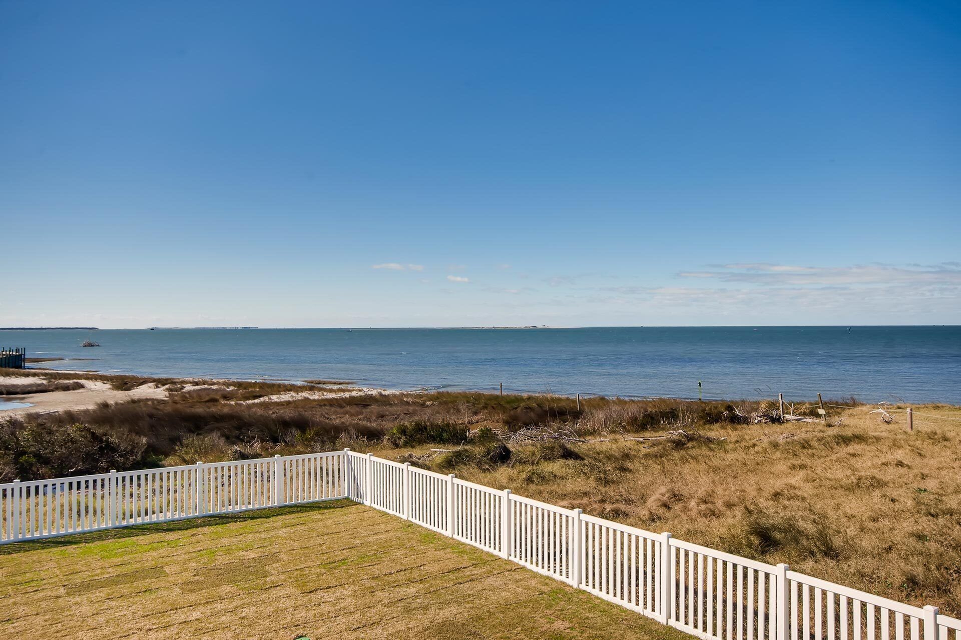 A coastal view with a white fence, grassy area, and a clear blue sky.