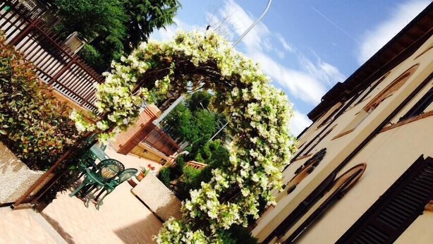 A narrow street with a building on the right, a wooden fence, and a garden with white flowers. - Hotel 2000 Fabriano (Fabriano)