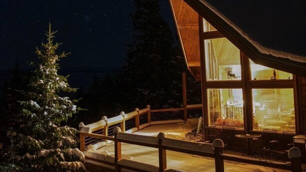 A cabin with a large glass window, wooden deck, and snow-covered ground. - Breath Taking Views-Near Yellowstone New Hot Tub.  Just off Union Pass! (Dubois)