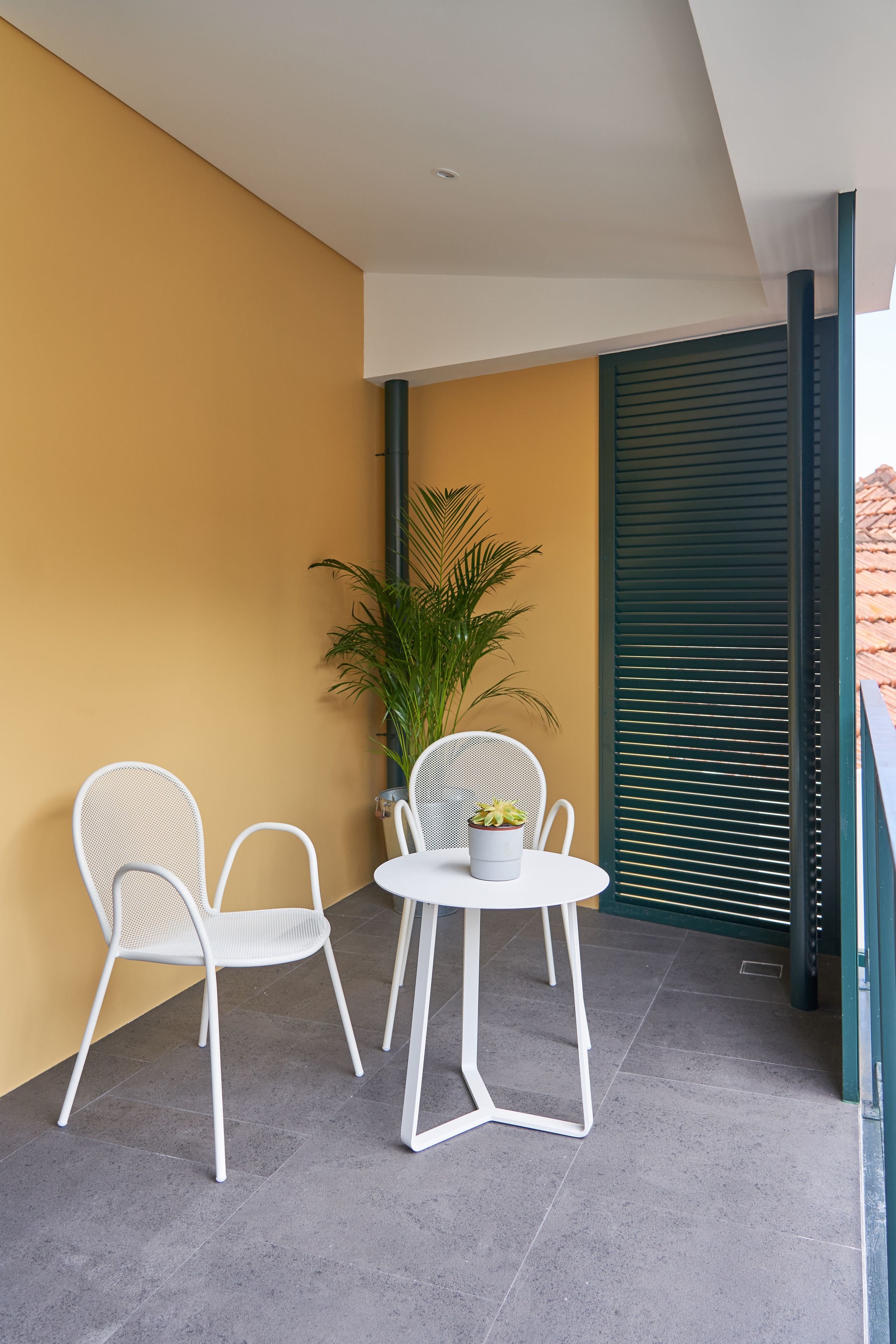 A balcony with two white chairs, a small round table, and a potted plant.
