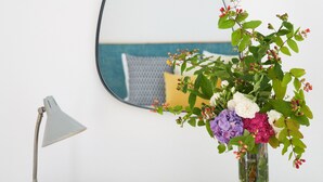 A wooden dresser with a mirror, a lamp, and a vase of flowers. - Good Memories Lodge (Funchal)