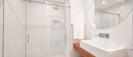 A modern bathroom with a glass-enclosed shower, a white sink, and a wooden vanity.