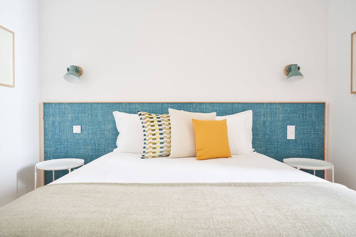 A neatly made bed with a blue headboard, white bedding, and two round side tables.