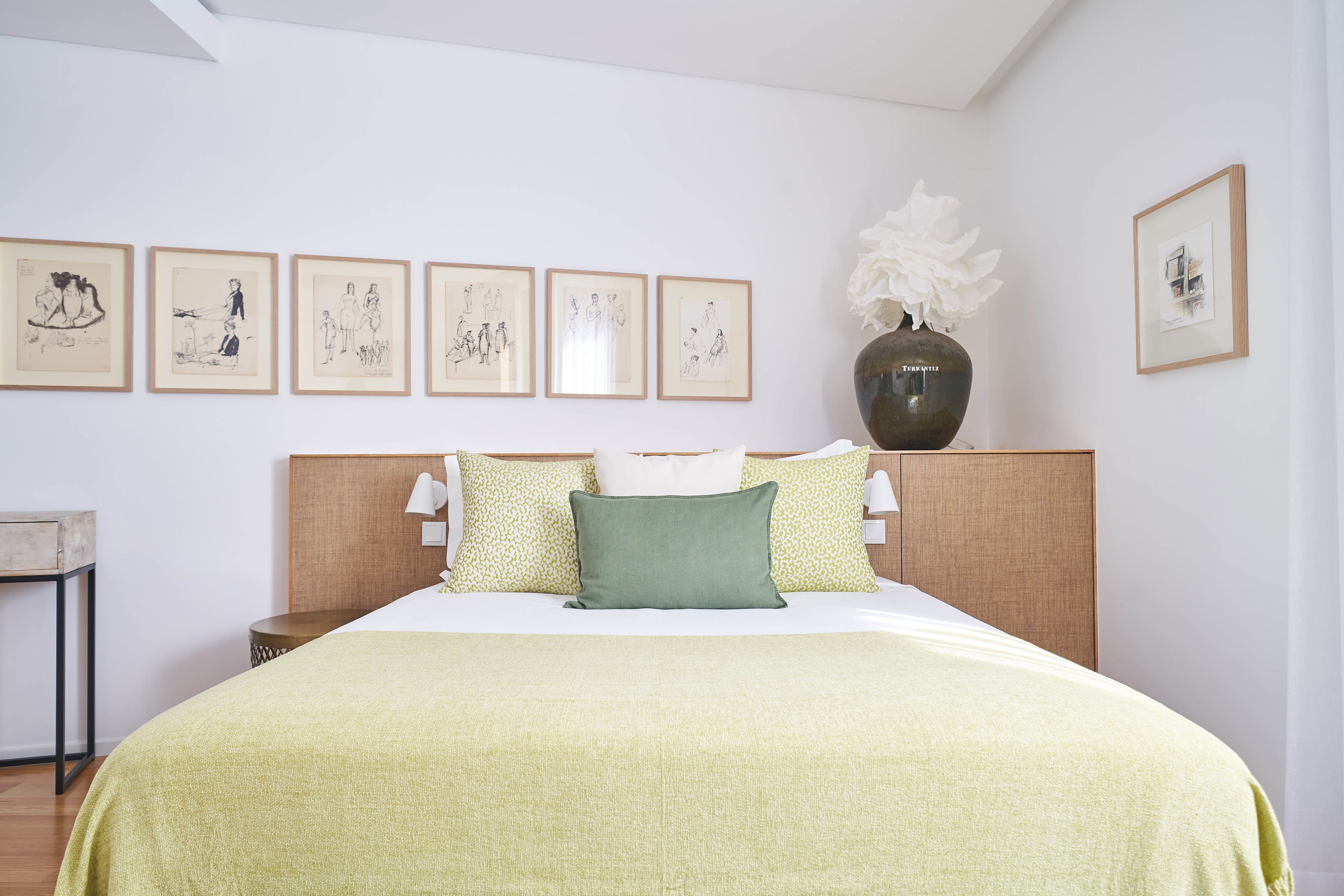 Ein ordentlich eingerichtetes Hotelzimmer mit einem großen Bett, einem Nachttisch, einer Lampe und einer Vase mit Blumen.
