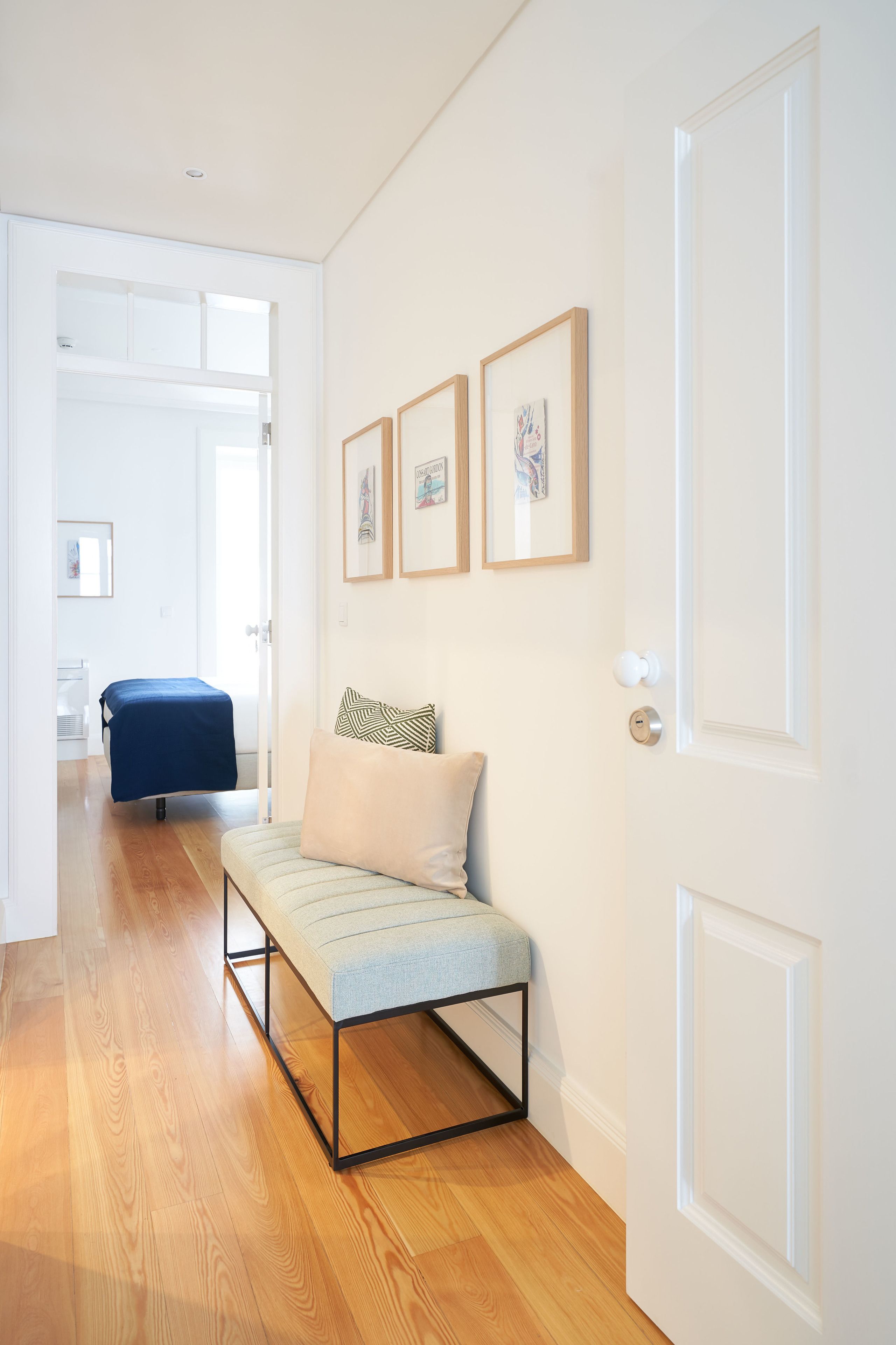 A hallway with a bench, a bed, and framed pictures on the wall.