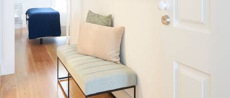 A hallway with a bench, a bed, and framed pictures on the wall.