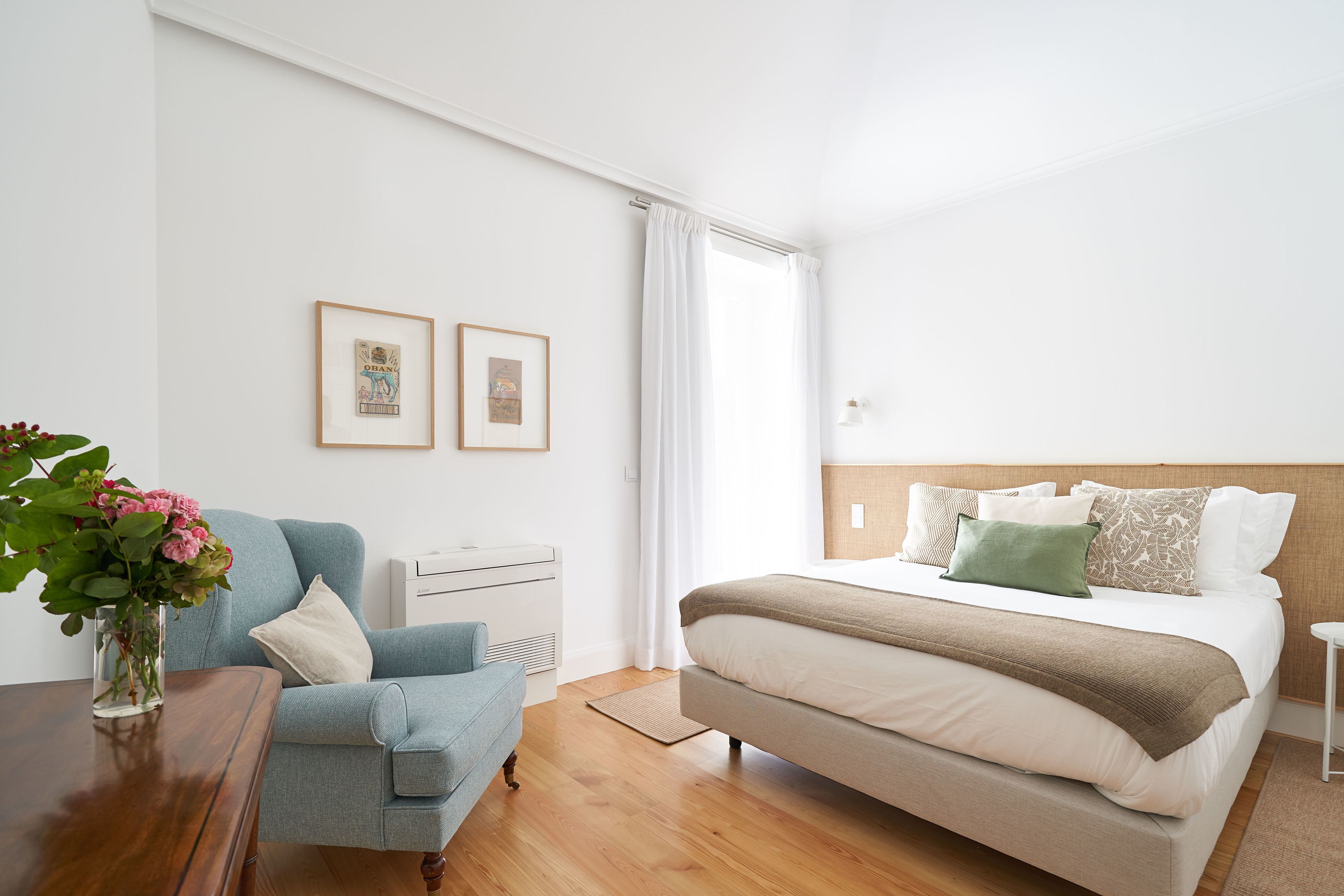 Ein Schlafzimmer mit einem Bett, einem Sessel, einem Tisch mit Blumen und zwei gerahmten Bildern an der Wand.