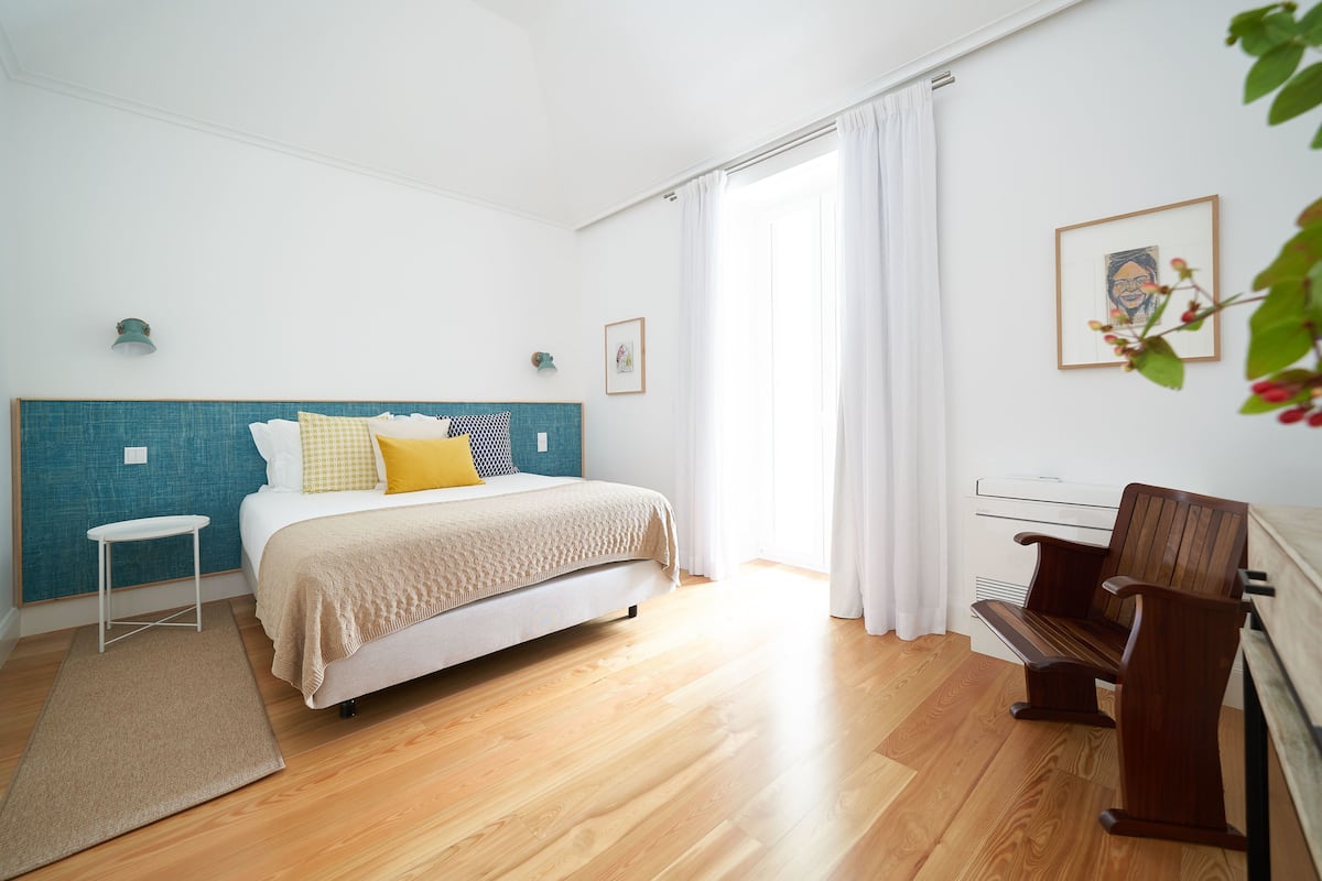 A bedroom with a bed, a chair, a small table, and a window with curtains.