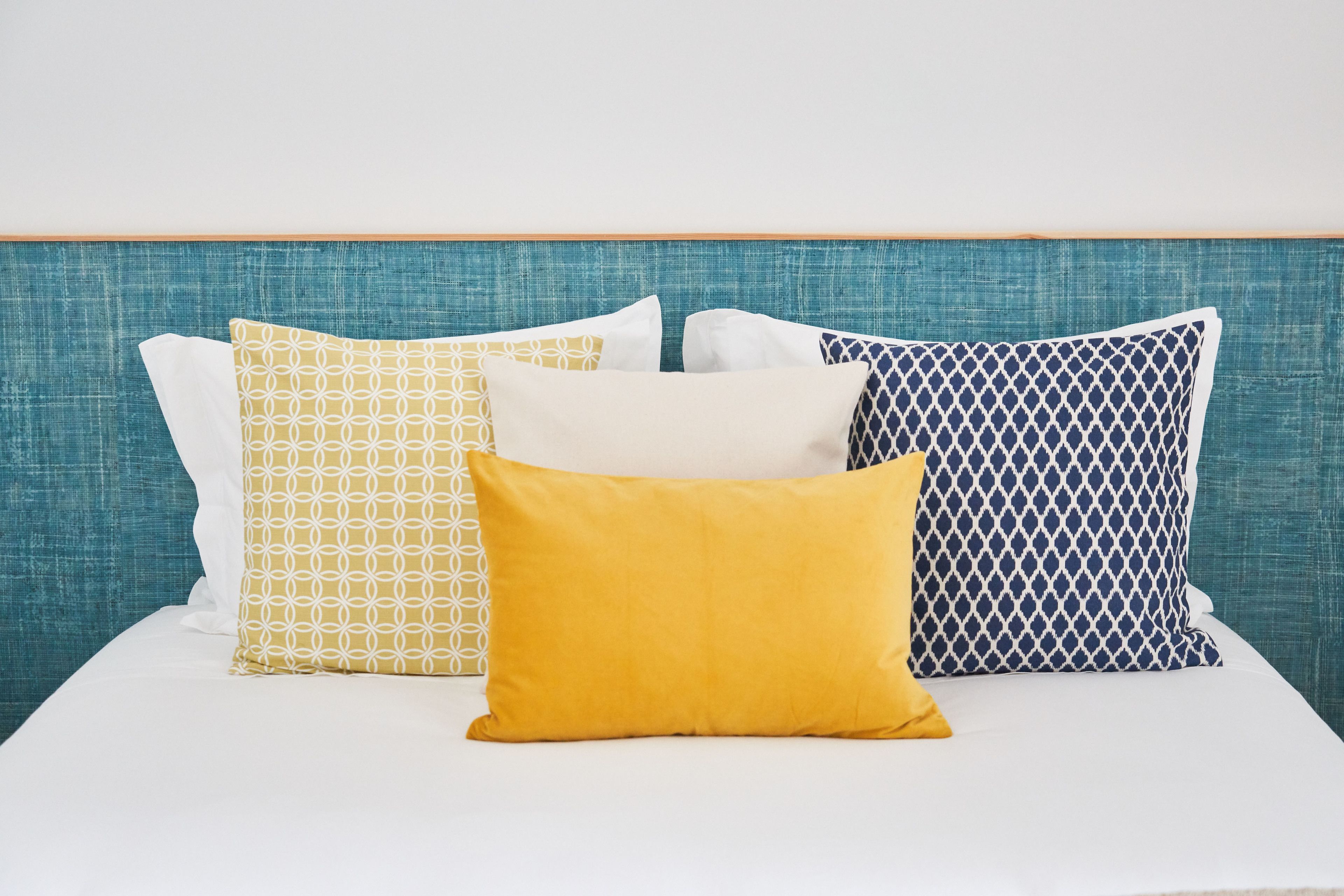 A bed with a teal headboard and four pillows in different patterns.