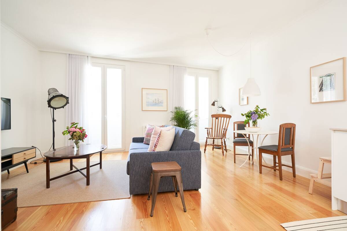 A spacious living area with a sofa, a small table, a chair, and a dining table with chairs.