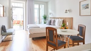 A modern bedroom with a bed, bedside table, and a dining area with chairs and a table. - Good Memories Lodge (Funchal)