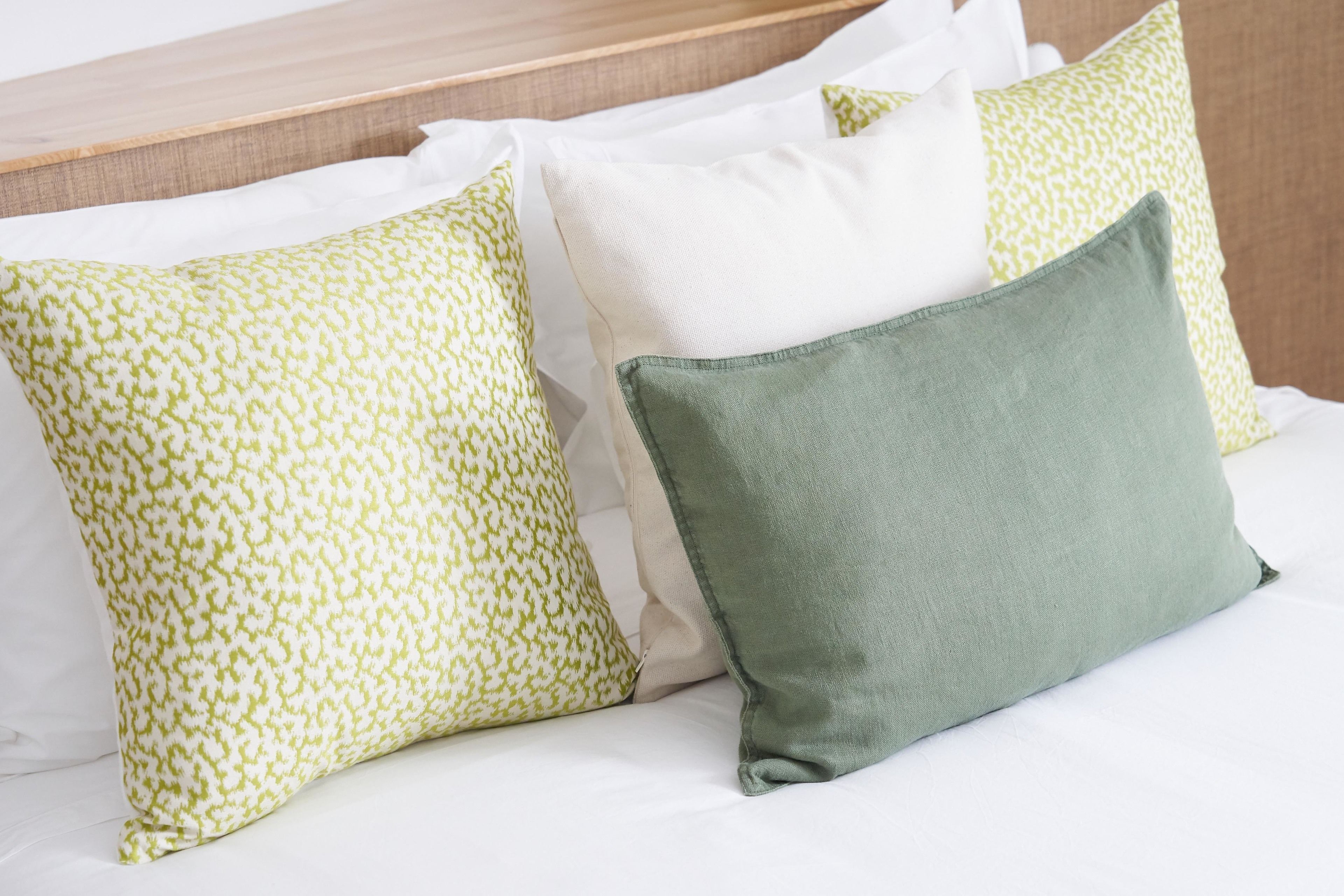 Un lit avec des draps blancs et trois oreillers aux motifs et aux couleurs différents.