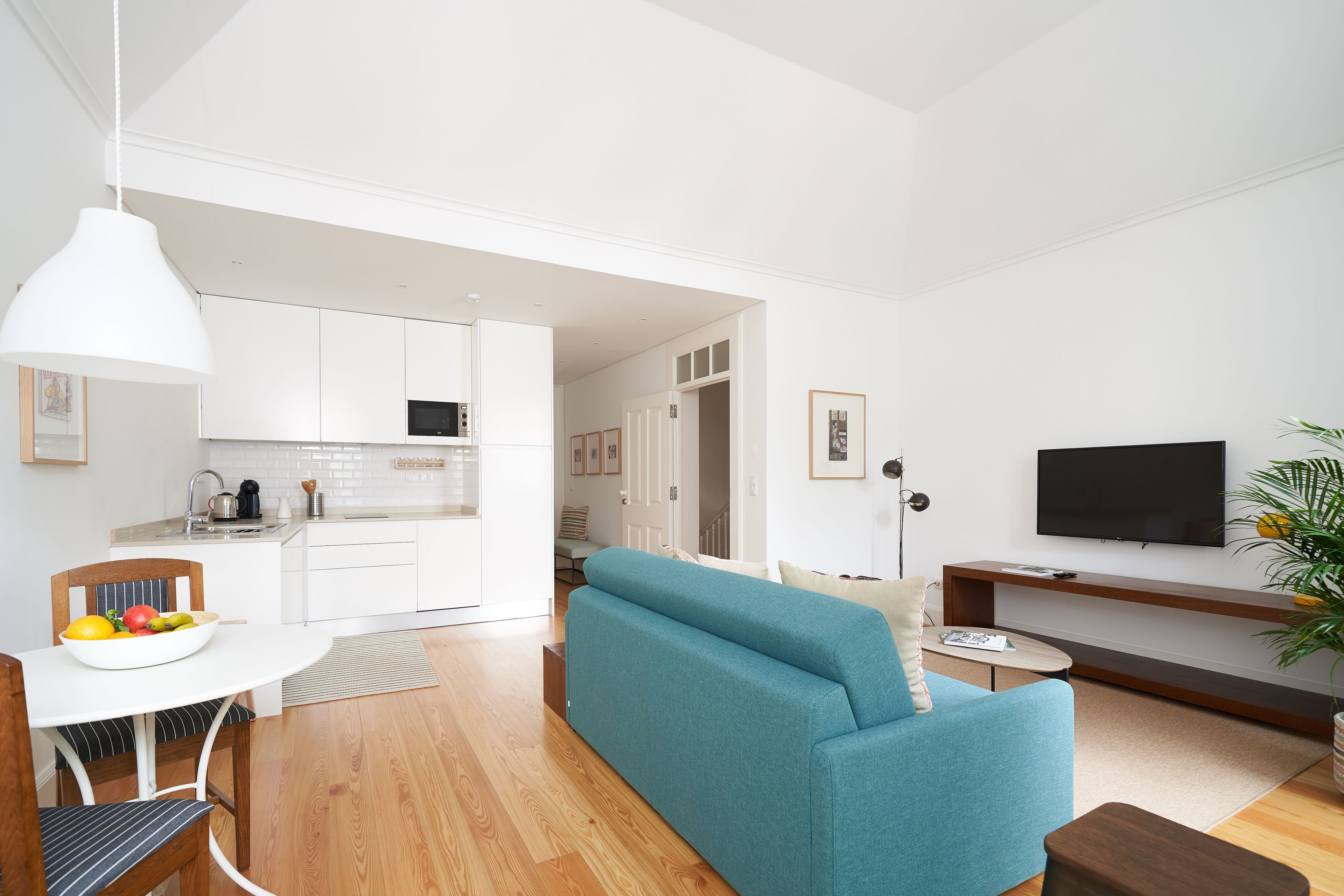 A modern living room with a teal sofa, a flat-screen TV, and a kitchen in the background.
