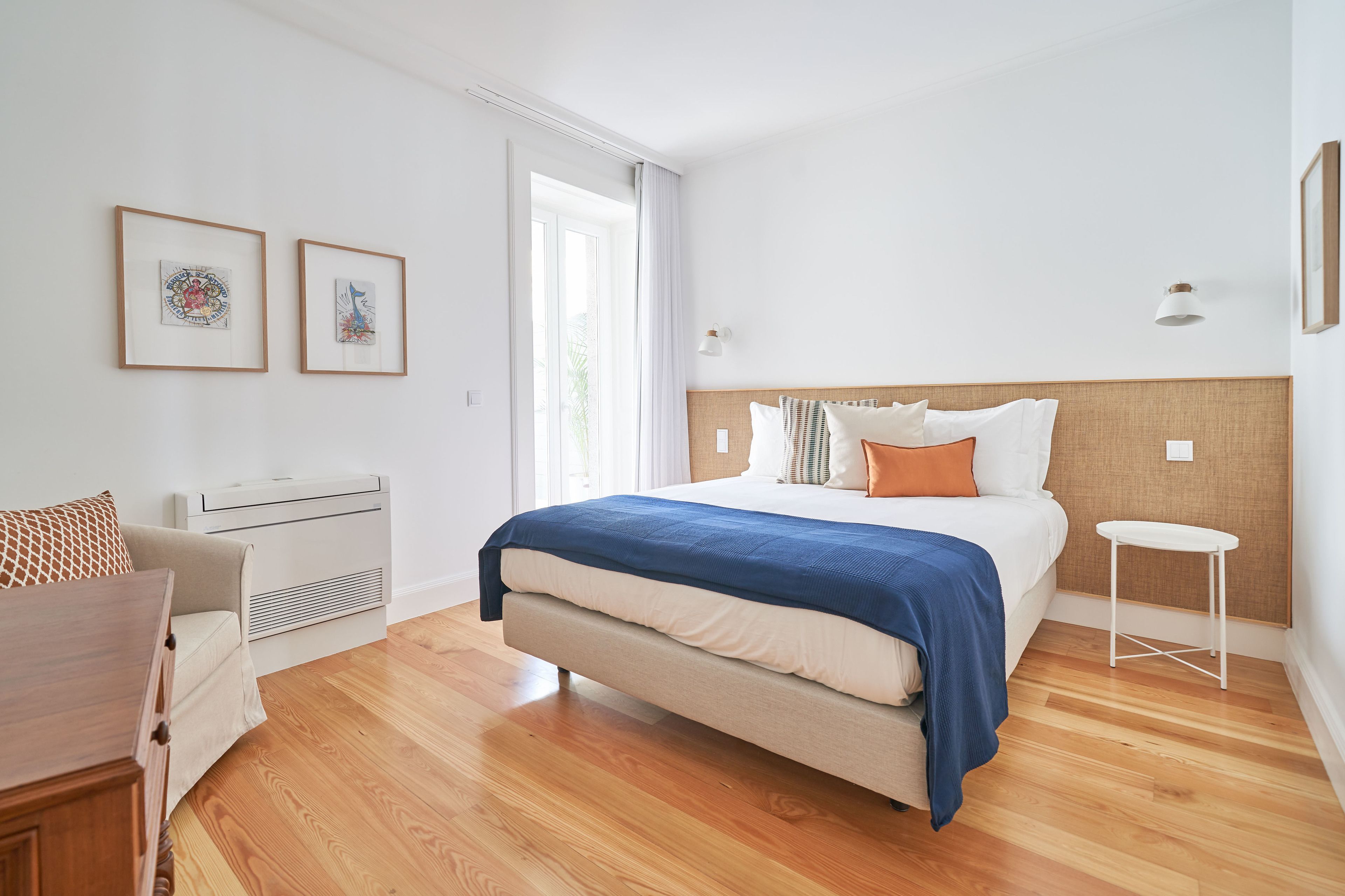 Ein modernes Schlafzimmer mit einem Bett, einem Sessel, einem kleinen Tisch und zwei gerahmten Bildern an der Wand.