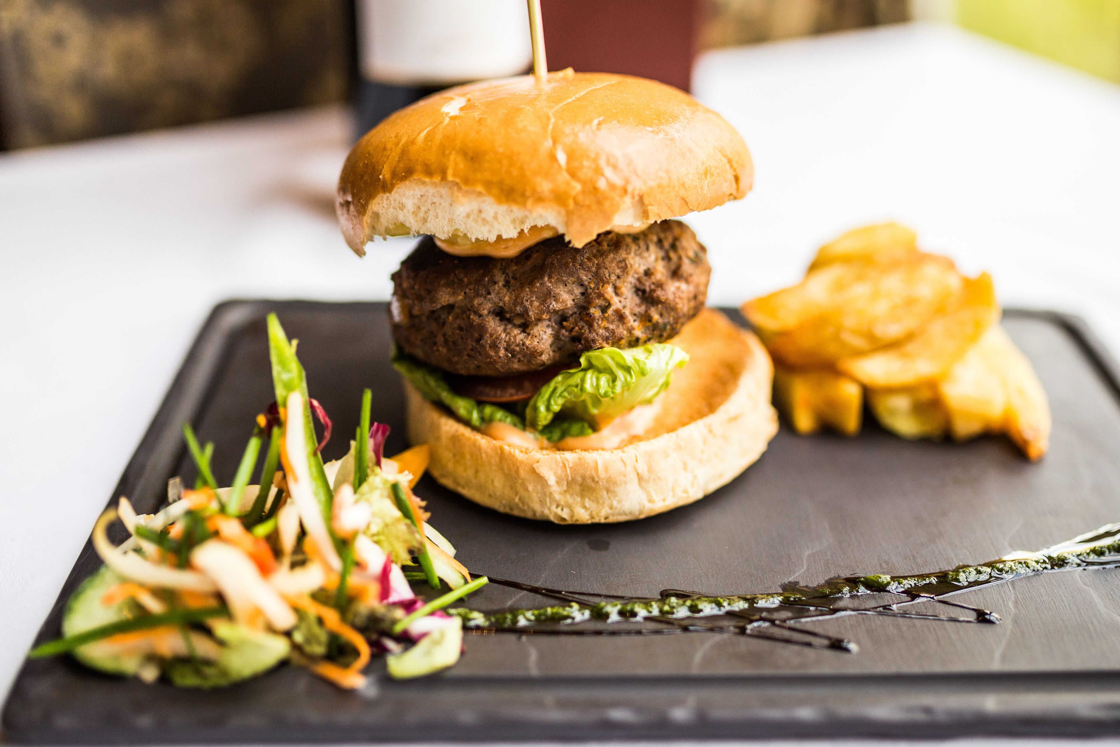 A burger with a toothpick, fries, and a side salad on a slate plate.