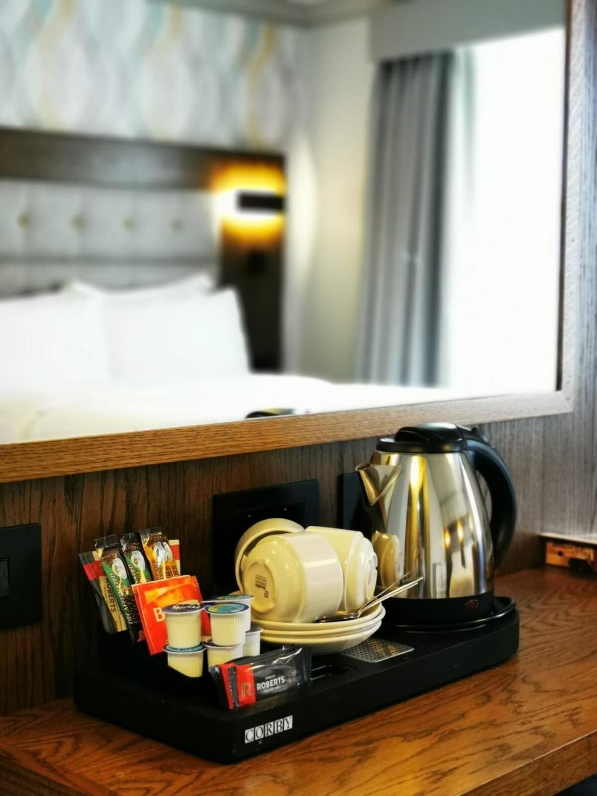 A hotel room with a wooden side table holding a coffee maker, tea bags, and a bottle of water.