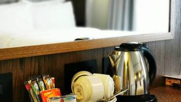 A hotel room with a wooden side table holding a coffee maker, tea bags, and a bottle of water.
