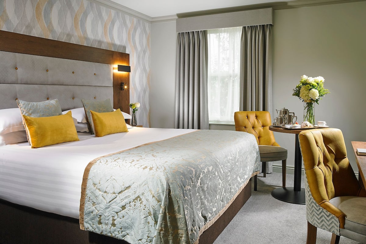 A hotel room with a large bed, a wooden headboard, a small table with a vase of flowers, and a chair.